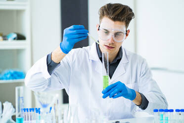 Young scientist mixing chemicals in graduated cylinder at laboratory - GIOF11542