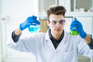 Male scientist holding chemical flasks in laboratory - GIOF11543