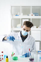 Male scientist filling flask with medicine through funnel in laboratory during COVID-19 - GIOF11555