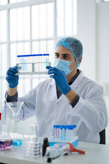 Männlicher Wissenschaftler hält Reagenzglasgestell im Labor während COVID-19 - GIOF11559