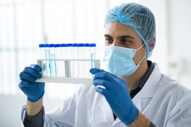 Männlicher Wissenschaftler mit Gesichtsschutzmaske bei der Untersuchung einer Chemikalie in einem Reagenzglas im Labor - GIOF11560