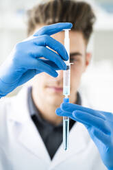 Männlicher Wissenschaftler, der eine Flüssigkeit in einem Reagenzglas mit einer Spritze im Labor mischt - GIOF11570