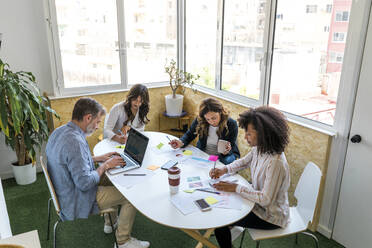 Male and female colleagues sitting at table while working in office - AFVF08334