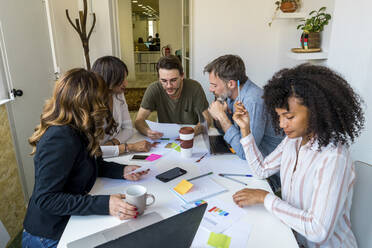 Multi-ethnic coworkers discussing while sitting at desk in office - AFVF08361