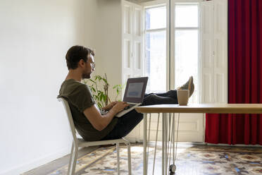 Junger männlicher Unternehmer arbeitet am Laptop, während er am Tisch im Büro sitzt - AFVF08370