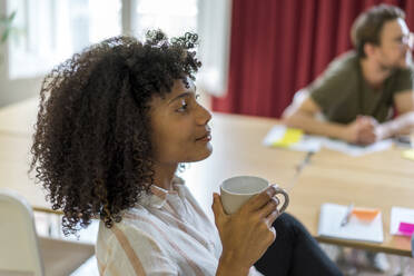 Young Afro female entrepreneur holding mug during meeting at office - AFVF08398