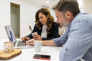 Männliche und weibliche Unternehmer planen ihre Strategie am Laptop, während sie in der Lobby ihres Büros sitzen - AFVF08422