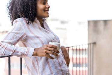 Smiling young female entrepreneur leaning on railing during coffee break at office - AFVF08426