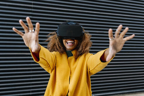 Cheerful woman watching video through wearable computer against wall - EGAF01977