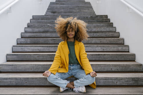 Afro woman in lotus position sitting on staircase - EGAF02008