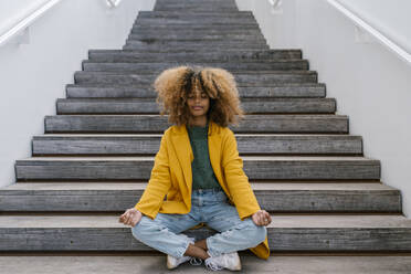 Afro woman meditating while sitting on staircase - EGAF02009