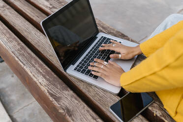 Frau benutzt Laptop auf einer Bank sitzend - EGAF02013