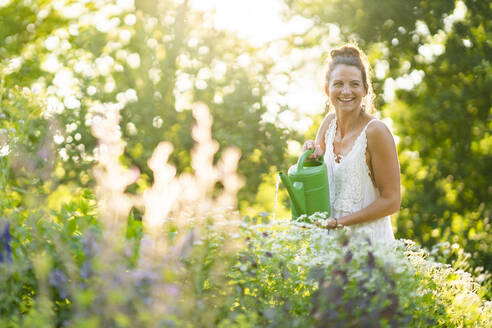 Portrait of young woman watering flowers in springtime garden - AKLF00106