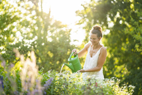 Young woman watering flowers in springtime garden - AKLF00107