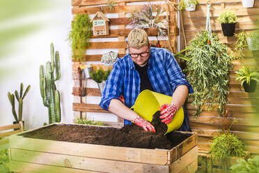 Junger Mann bereitet das Substrat für einen städtischen Garten aus Paletten auf seiner Terrasse vor - RTBF01565