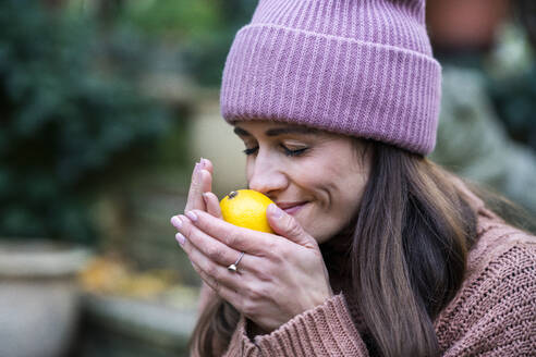 Portrait of beautiful woman wearing pink knit hat smelling fresh lemon with closed eyes - AKLF00110