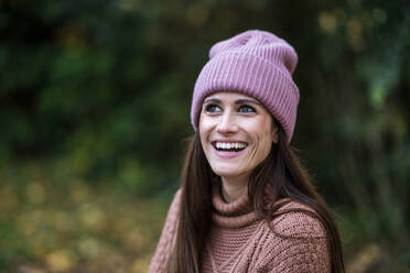 Portrait of beautiful woman wearing pink knit hat standing outdoors and smiling - AKLF00114