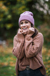 Portrait of beautiful woman wearing pink knit hat and sweater standing outdoors and smiling - AKLF00115