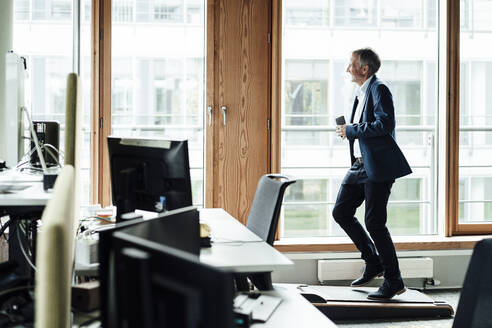 Lächelnder Geschäftsmann schaut weg, während er auf dem Laufband im Büro trainiert - GUSF05356