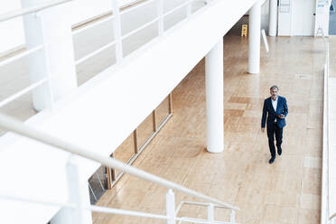 Businessman with digital tablet walking in office corridor - GUSF05358