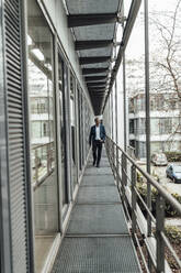 Businessman looking away while walking in office balcony - GUSF05382