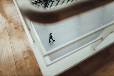 Businessman with digital tablet walking in corridor at office - GUSF05396