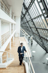 Senior businessman using digital tablet while walking on staircase - GUSF05398