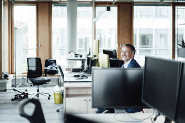 Smiling businessman sitting amidst computers in office - GUSF05430