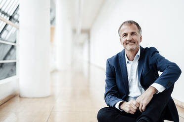 Smiling businessman sitting on floor in office cafeteria - GUSF05452