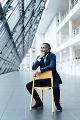 Senior Business Professional mit Hand auf dem Kinn sitzt auf einem Stuhl im Flur im Büro - GUSF05466