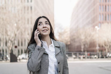 Mature businesswoman talking on smart phone while looking sideways in city - JCZF00471