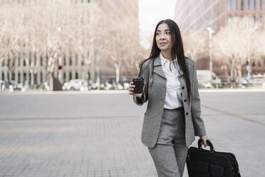 Nachdenkliche reife Geschäftsfrau mit Tasche, die eine Kaffeetasse hält, während sie in der Stadt wegschaut - JCZF00472