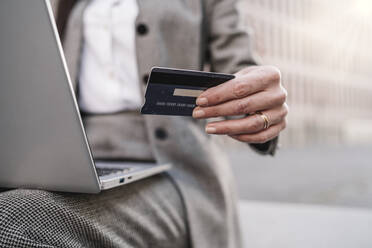 Businesswoman using credit card and laptop while sitting outdoors - JCZF00478