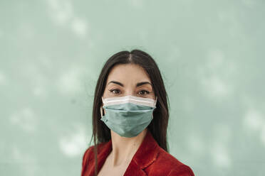 Businesswoman with protective face mask against turquoise wall during COVID-19 - JCZF00492