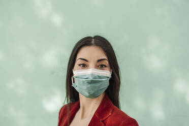 Geschäftsfrau mit Gesichtsschutzmaske vor türkisfarbener Wand während COVID-19 - JCZF00492
