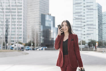 Geschäftsfrau, die beim Gehen in der Stadt mit ihrem Smartphone telefoniert - JCZF00499