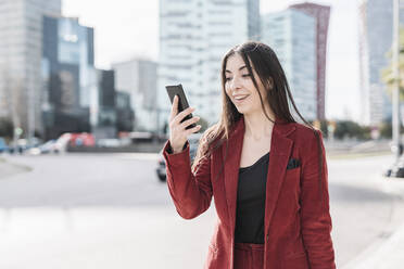 Überrumpelte Geschäftsfrau, die auf ihr Smartphone schaut, während sie in der Stadt steht - JCZF00500
