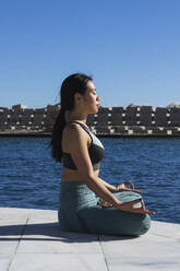 Sportswoman meditating while practicing lotus position on promenade during sunny day - PNAF00893