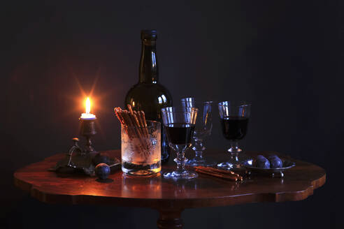 Studioaufnahme einer Flasche Rotwein, drei gefüllte Weingläser, Pflaumen, salzige Brezeln und eine brennende Kerze auf einem kleinen Couchtisch - JTF01819