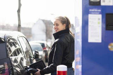 Porträt einer jungen, schönen Blondine, die ihr Auto an einer Tankstelle auftankt - SGF02784