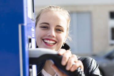 Porträt einer jungen schönen Blondine, die an einer Tankstelle mit einer Zapfsäule in der Hand posiert - SGF02791