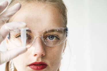 Portrait of beautiful woman wearing protective goggles holding vial - SGF02798
