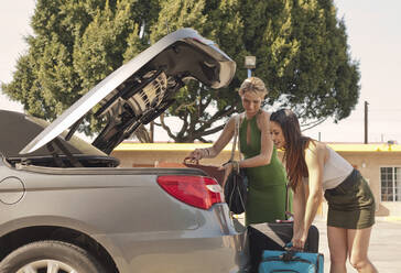 Junge Frauen laden an einem sonnigen Tag Gepäck in den Kofferraum eines Autos - AJOF01163