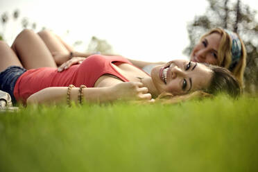 Schöne fröhliche Frau mit Freundin auf Gras im Park liegend - AJOF01174