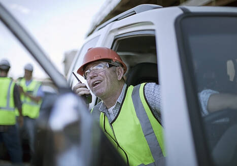 Portrait of construction worker sitting in car and talking on walkie-talkie - AJOF01180
