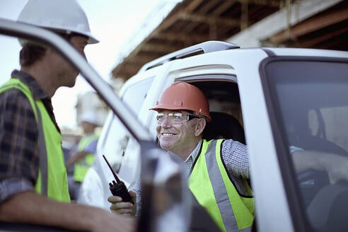 Two male construction workers chatting by car - AJOF01181
