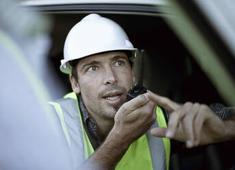 Porträt eines Bauarbeiters, der im Auto sitzt und mit einem Funkgerät spricht - AJOF01187