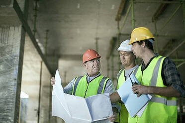 Männliche Bauarbeiter besprechen Pläne auf der Baustelle - AJOF01191