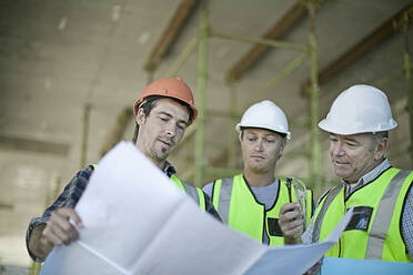 Male construction workers talking over plans at construction site - AJOF01194