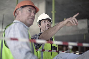 Zwei männliche Bauarbeiter unterhalten sich auf einer Baustelle - AJOF01195